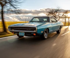 Vintage car driving down a scenic road with clear skies.