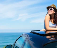 A woman sitting on top of her car, enjoying the view of the sea