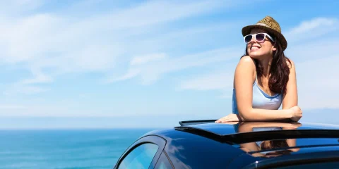 A woman sitting on top of her car, enjoying the view of the sea