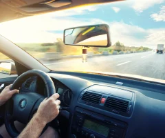 Close-up of hands gripping the steering wheel while driving on the road.