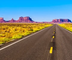 A scenic road stretching toward distant mountains, with a clear sky above.