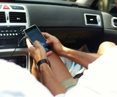 A man holding his cellphone for navigation while driving inside a car