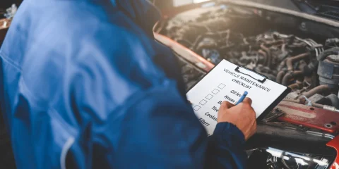 A mechanic checking a list while inspecting a car in a garage