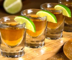 Four tequila shots lined up on a bar counter, with a vibrant lime wedge and salt