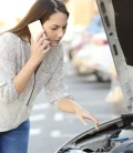 A person on the phone calling for help after their car breaks down on the side of the road.