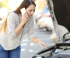 A person on the phone calling for help after their car breaks down on the side of the road.