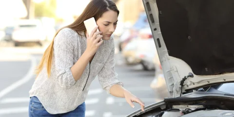 A person on the phone calling for help after their car breaks down on the side of the road.