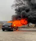 A car on fire on the side of the road, with thick smoke rising from the vehicle