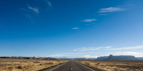 A lonely, empty road stretching into the horizon, surrounded by scenic landscapes.