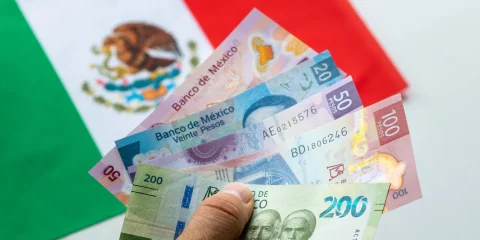 Imagen de billetes mexicanos con la bandera mexicana de fondo.