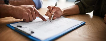 A person carefully filling out a claims document with a pen