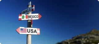 A photo of road signs indicating the direction to Mexico and the USA, with arrows pointing to each country.